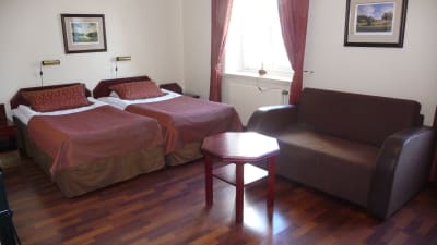 Ett anonymt hotellrum. Två sängar, en soffa och ett bord.