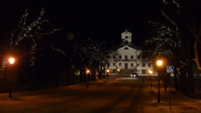 Julbelysning pryder ljusen längs med en gata i Kristinestad. I bakgrunden syns ett vitt stort hus.