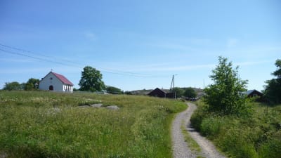 En skärgårdsby med en väg genom en äng och en vit kyrka i bakgrunden