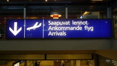 En blå skylt med texten "Ankommande flyg" på finska, svenska och engelska.