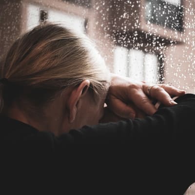 nainen nojaa päätänsä sateiseen ikkunaan.