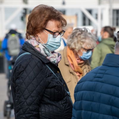 Iäkkäät ihmiset, joilla on suoja maskit Helsingin silakkamarkkinoilla. 
