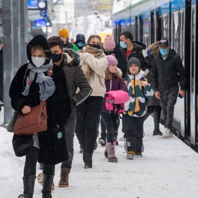 Vinterklädda passagerare på tågperrong i snöväder. 