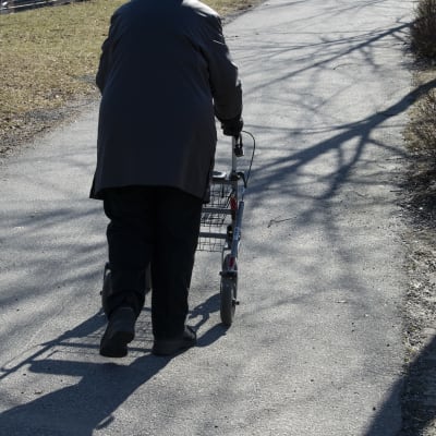 En äldre person går ute med en rullator.