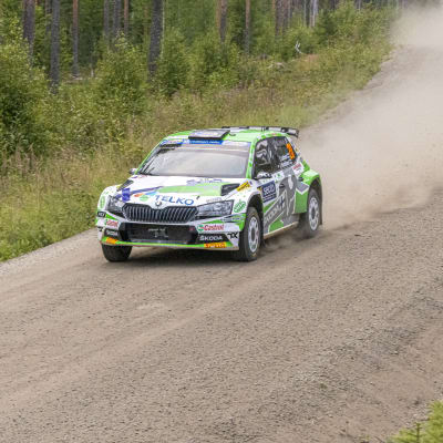 En rallybil susar i hög fart på en grusväg.