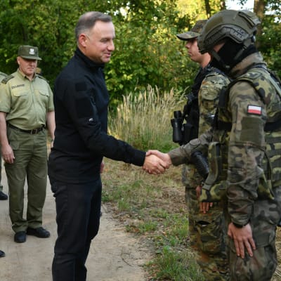 Polens president, klädd i helsvart, skakar hand med två soldater i camouflageuniformer.