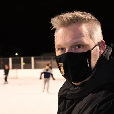 En man med svart munskydd vid en ishockeyrink utomhus.