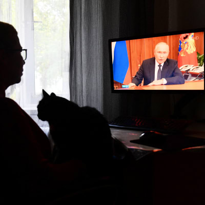 En person som ser på en tv, där ett tal med Vladimir Putin sänds.