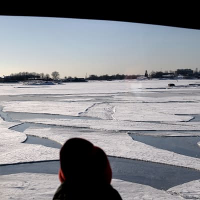 Henkilö katsoo jäätynyttä Suomenlahtea lautalla.