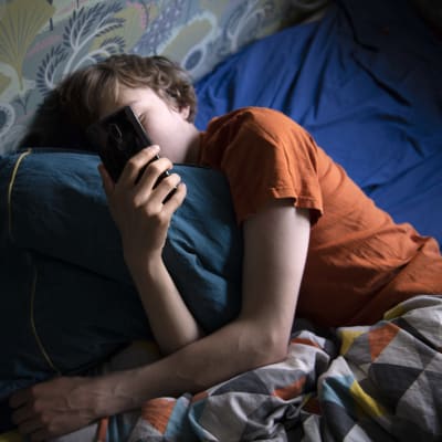 Pojke ligger i sängen med telefonen i handen.