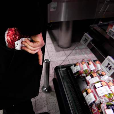 Henkilö laittaa ruokakaupassa lihapaketin taskuunsa.