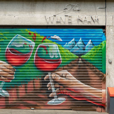 Katutaidetta Dublinissa: The Wine Pair -viinikaupan ja -baarin ikkuna on peitetty metalliverholla, johon on maalattu kaksi punaviinilasilla kilistelevää kättä.