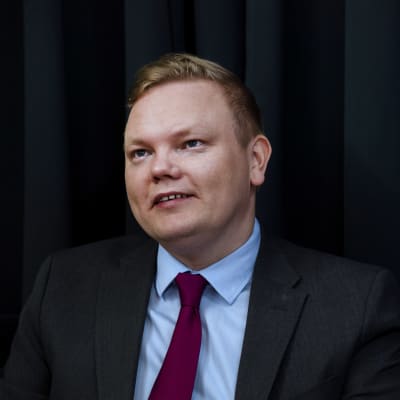 En blond man i svart kostym.