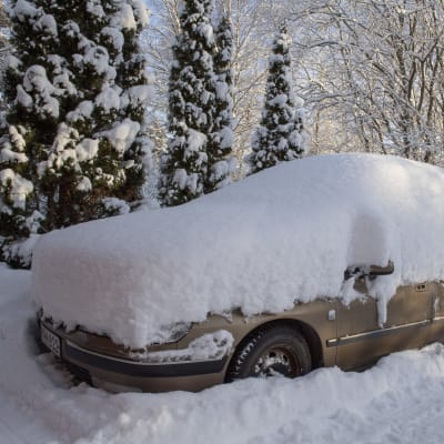 Talvisessa pihapiirissä parkkeerattu auto on hautatutunut lumikerroksen alle.