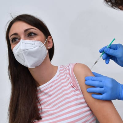 En kvinna i munskydd får coronavaccin av en sjukskötare.