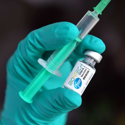 Närbild på Pfizer-Biontechs coronavaccin och en spruta.