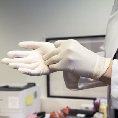 Närbild på händer. En läkare drar på sig handskar.