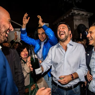 Matteo Salvini står med en Champagneflaska i handen och ser strålande glad ut.