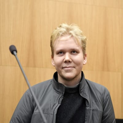 Aleksanteri Kivimäki är en blond ung man med kort hår. Han sitter i rätten och ler.