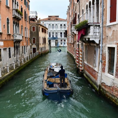 En båt i en kanal i Venedig, mellan två tegelstensbyggnader.
