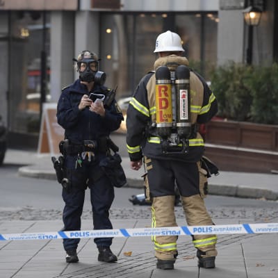 Polis med gasmask och brandman står innanför det avgränsade området i Östermalm där ett företag tagit emot en försändelse innehållande pulver.