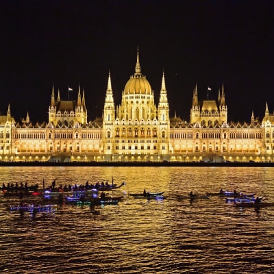 Unkarin parlamenttitalo kirkkaasti valaistuna pimeässä illassa.