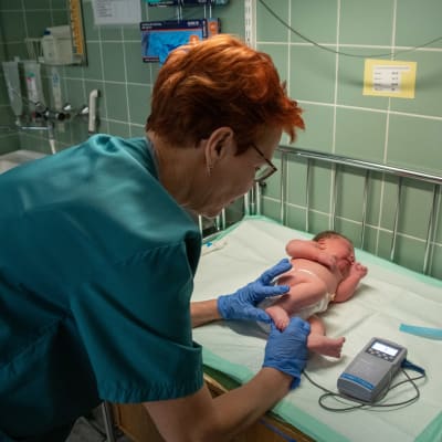 Barnmorskan Mervi Lanu mäter nyfödda Ronjas puls. Ronja ligger med blöja på skötbordet. 