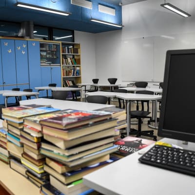 Böcker och laptop i förgrunden, tomt klassrum i bakgrunden