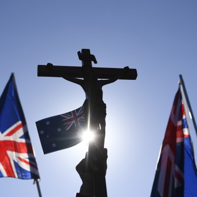 En hand som håller upp ett krucifix och två australiska flaggor