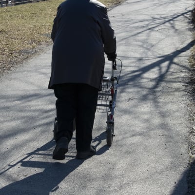 En äldre person går ute med en rullator.