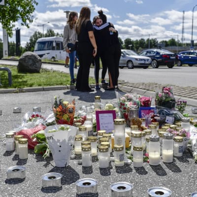 Flickor kramar och tröstar varandra framför ljus och blommor som förts till bensinstationen där en 12-årig flicka blev skjuten. 