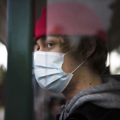 En person med munskydd står på busshållplatsen.