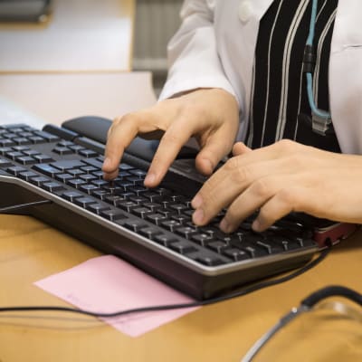 En person i läkarrock skriver på ett tangentbord.