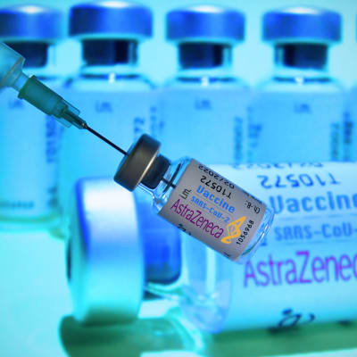 En person håller i en dos med AstraZenecas coronavaccin. I bakgrunden syns fler doser.