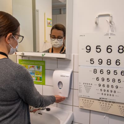 En skolhälsovårdare i munskydd står och tvättar händerna.