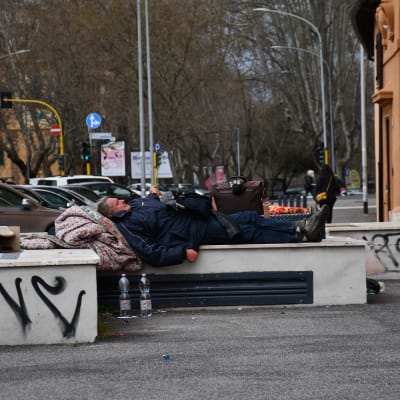 En hemlös man sover på en bänk i Italiens huvudstad Rom