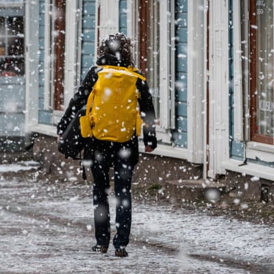 En kvinna promenerar längs en gata, det snöar