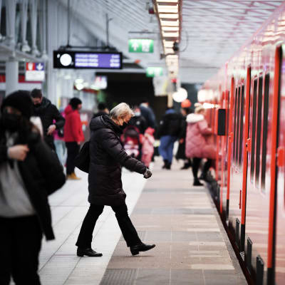 Människor i munskydd går vid en metro i Helsingfors.