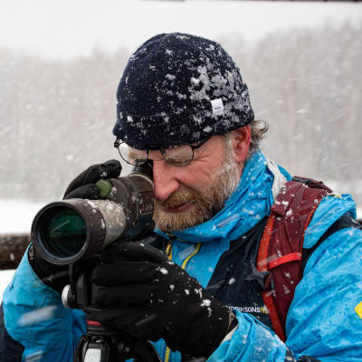 Pontus Rancken tittar i sin tubkikare. Snön yr omkring honom.
