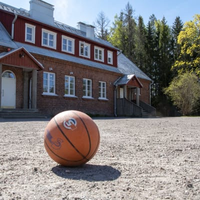 En baskeboll ligger på sandplanen framför Södra Paipis skola och förskola.