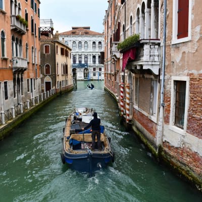 En båt i en kanal i Venedig, mellan två stegelstensbyggnader.