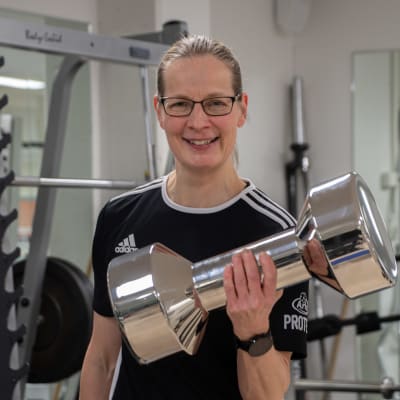 Eija Kolmonen är i konditionssalen. Hon håller i pokalen som ser ut som en jättestor hantel i silver.
