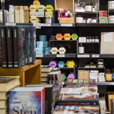 Affärshyllor med kosmetik och andra hälsoprodukter så som smoothiepulver. I förgrunden syns en mängd böcker som också är till salu.