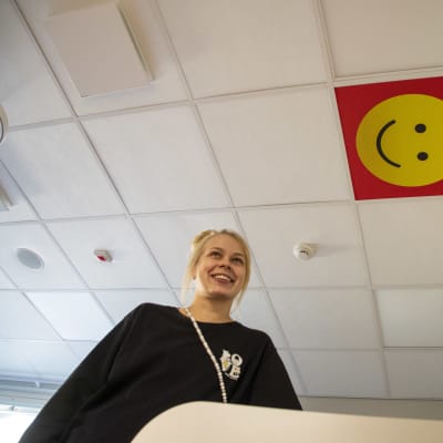 En kvinna står vid ett skötbord och i taket syns en glad smiley.
