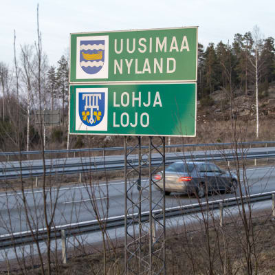 Motorväg vid Lojos stadgräns där det står Nyland och Lojo på svenska och finska på en skylt. En bil kör på motorvägen.