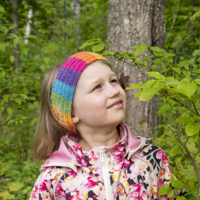 En sexårig flicka står i en träddunge, klädd i en blommig rock. Hon står och tittar på ett ungt träd.
