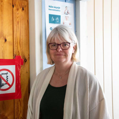 En vithårig kvinna står bredvid en skylt om telefonförbud.