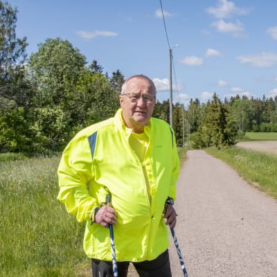 En man i reflexgul jacka står med sina vandringsstavar på en gång- och cykelväg. Han tittar in i kameran.