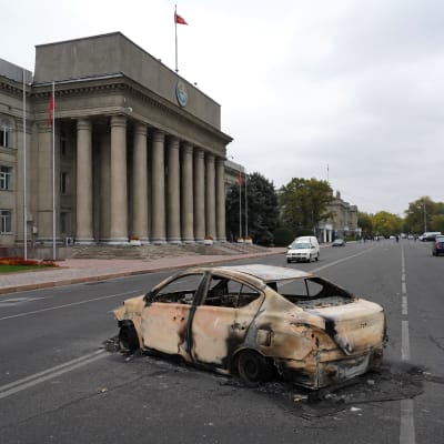 En utbränd bil på gatan framför en palatsliknande byggnad