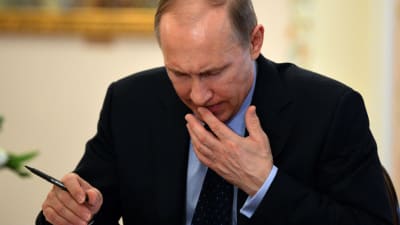 President Vladimir Putin läser dokument med en penna i ena handen samtidigt som han för andra handens fingrar till munnen.